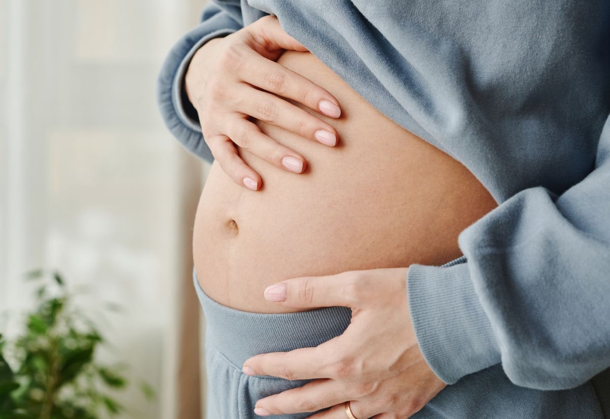 Face-free close-up of a pregnant woman in light-blue clothing cradling her bump
